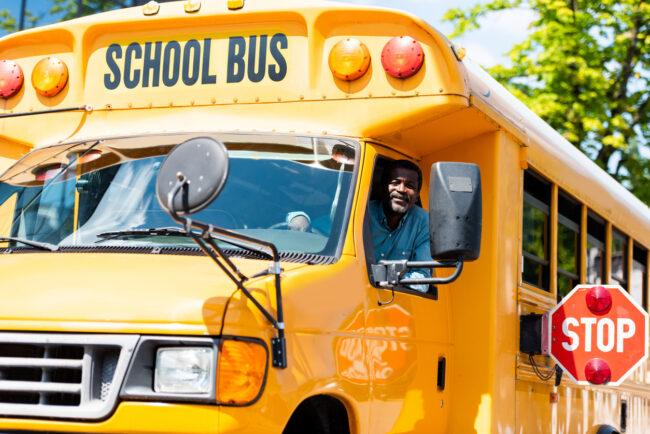 A school bus driver, leaning out of his open window, smiling.