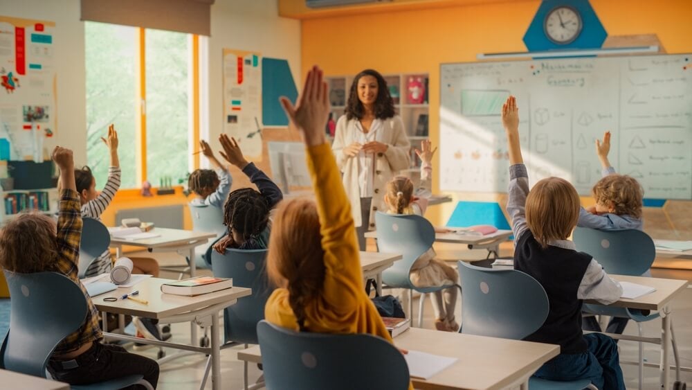 a teacher in the front of the classroom, with her students' hands raised